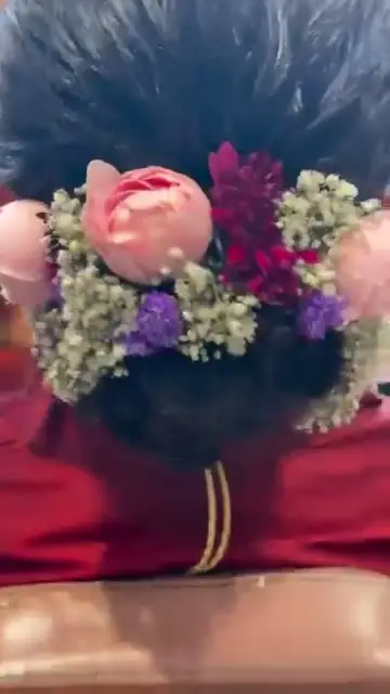 A cluster of fresh flowers - a pink rose, magenta and purple blooms and baby's breath - held above a red outfit.